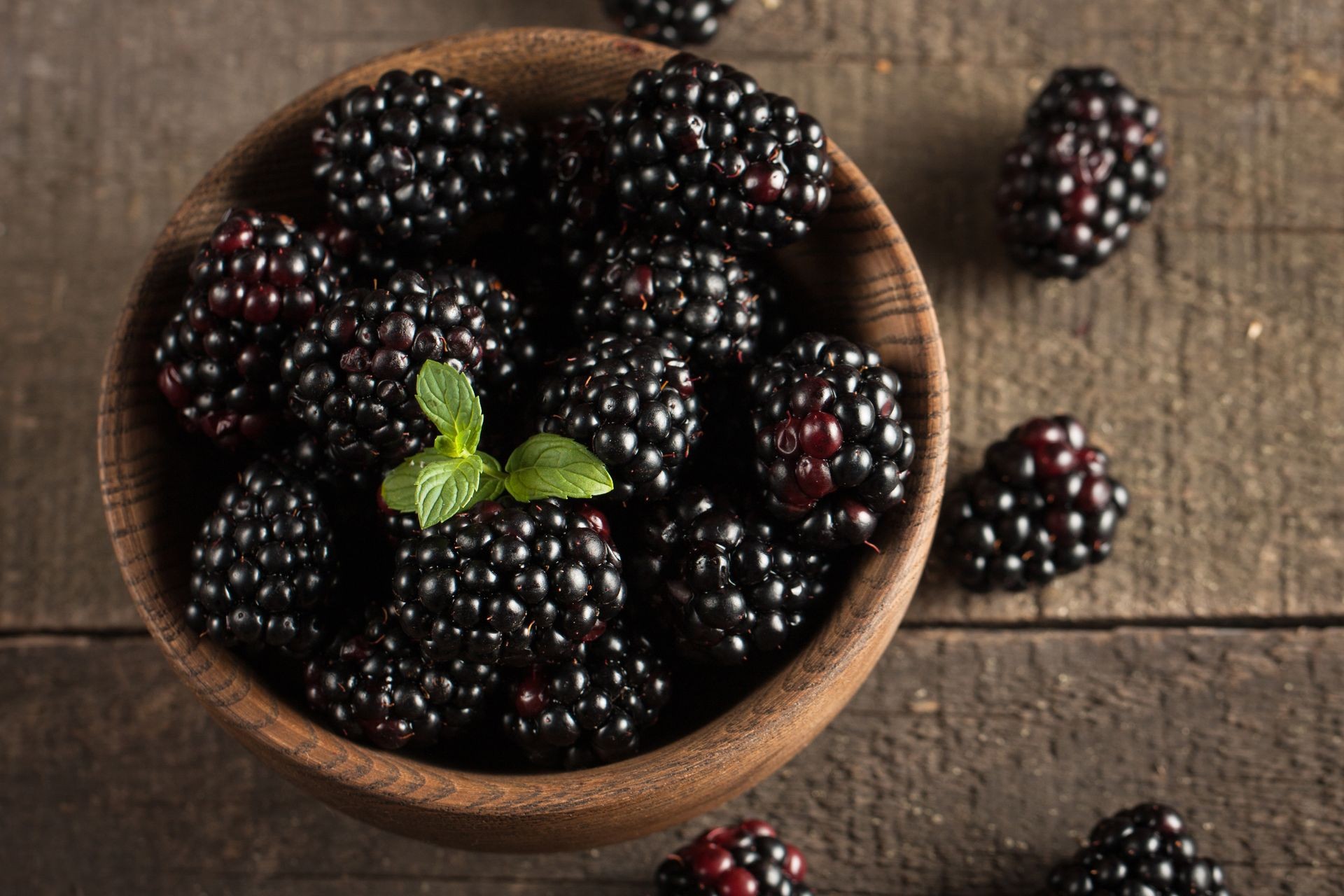 Fresh organic ripe blackberries in a wooden bowl on wooden background. Healthy rustic food concept.